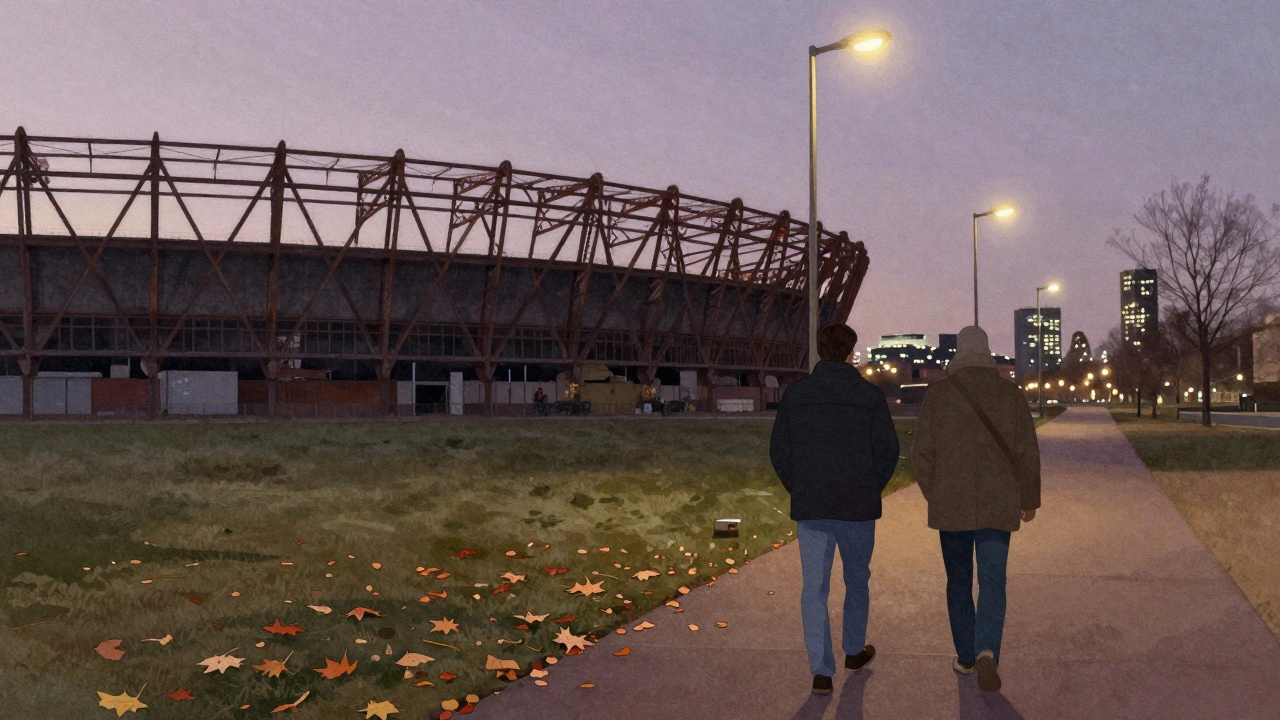 A companion walking through Olympic Park at dusk beside someone, past the old velodrome under a lavender sky.